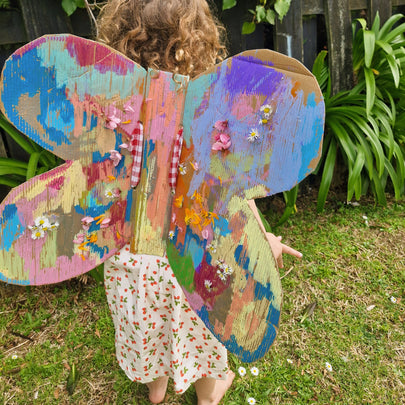 Child with a colorful butterfly costume standing outdoors in a garden.