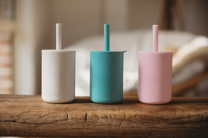 Three colorful cups with straws on a wooden surface