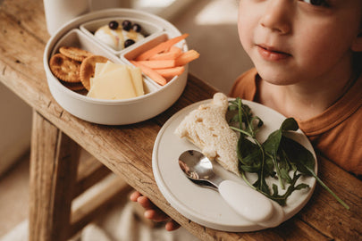 Child enjoying meal with 5 piece silicone dinnerware featuring a divided plate and healthy snacks.