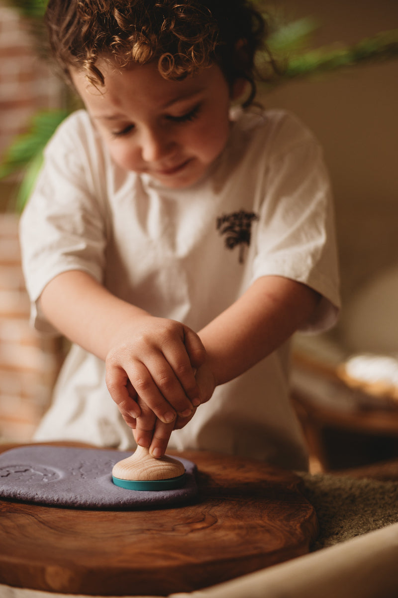 child playing with wooden dough stamper and dough for creative play