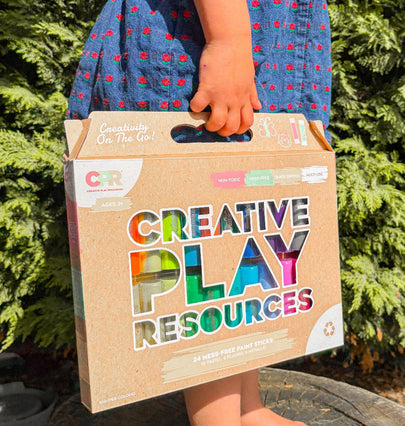 Child holding a 'Creative Play Resources' box outdoors