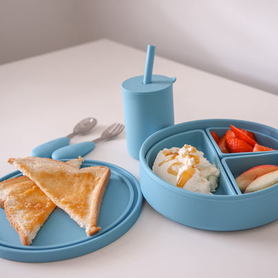 Blue children's meal set with plate, cup, and bowl on a white surface