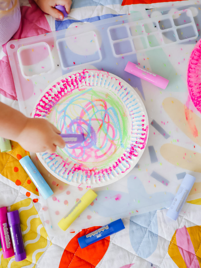child holding non-toxic paint sticks to draw on paper plate. creative play ideas for kids.