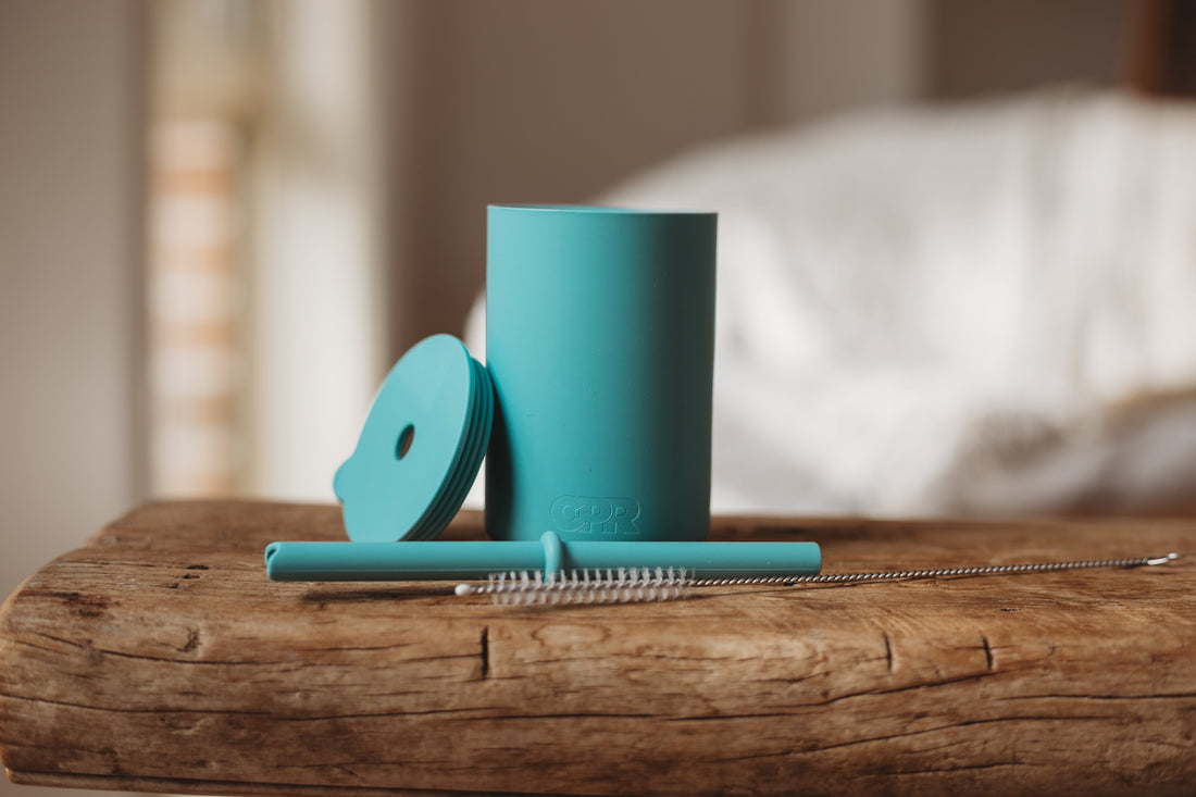 Silicone sippy cup with lid and straw and straw cleaner on a bench