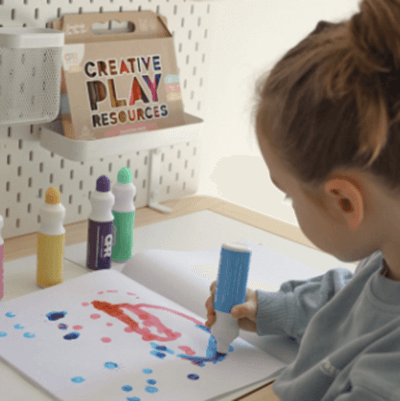 Child using play-based toys for Christmas gifts to create colorful art with markers and paper.