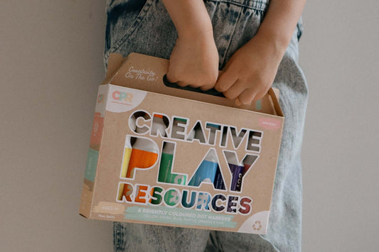 Child holding a box of creative play resources, featuring educational activities for kids with vibrant dot markers.