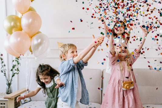 Boys and girls celebrating at a birthday party, laughing, and playing together with balloons and confetti.