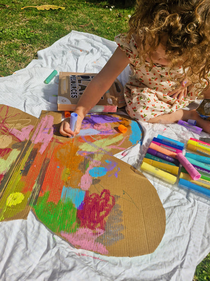 Child painting on a large cardboard with colored markers outdoors.