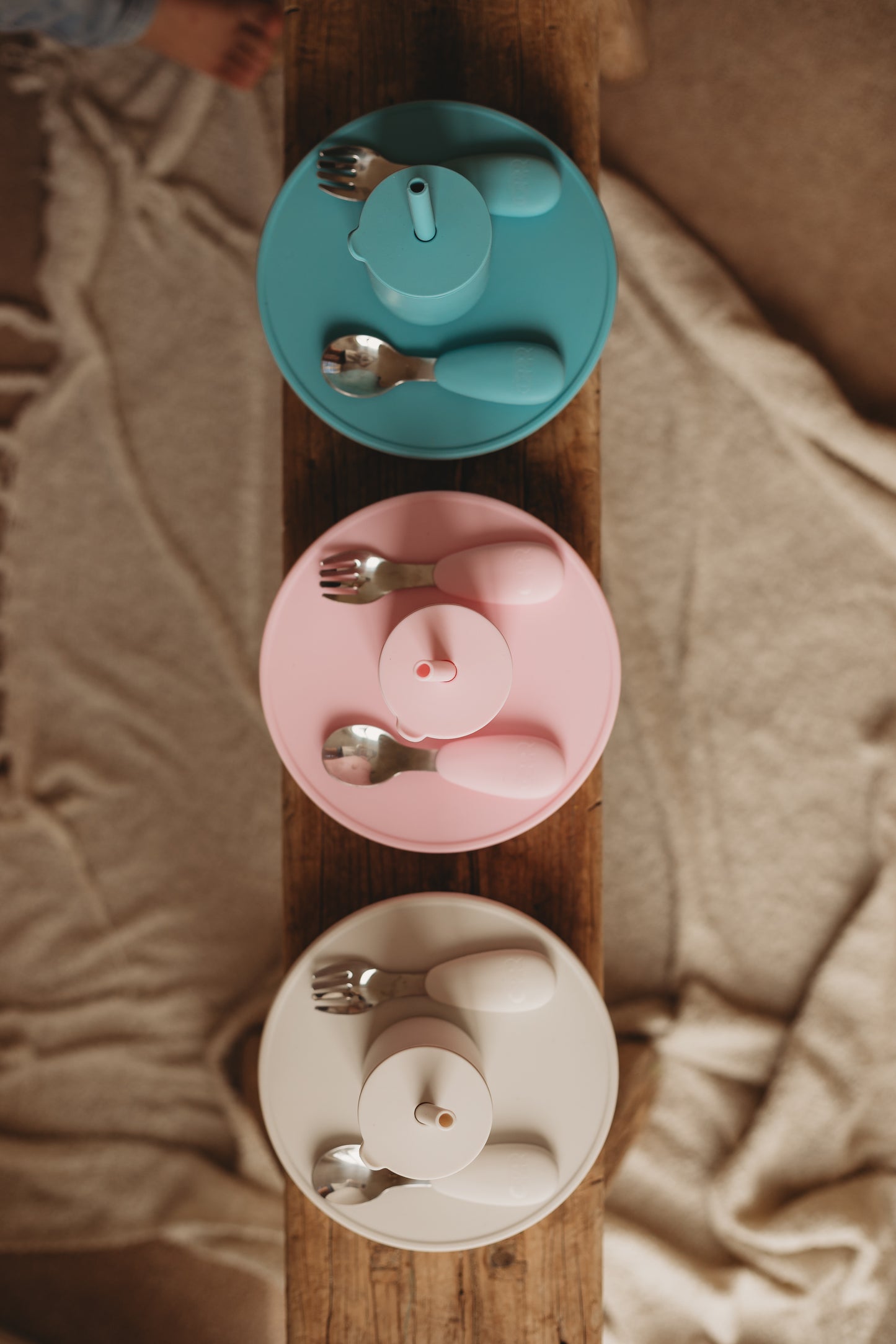 Set of colorful children's dinnerware including bowls, spoons, and forks on a wooden board.