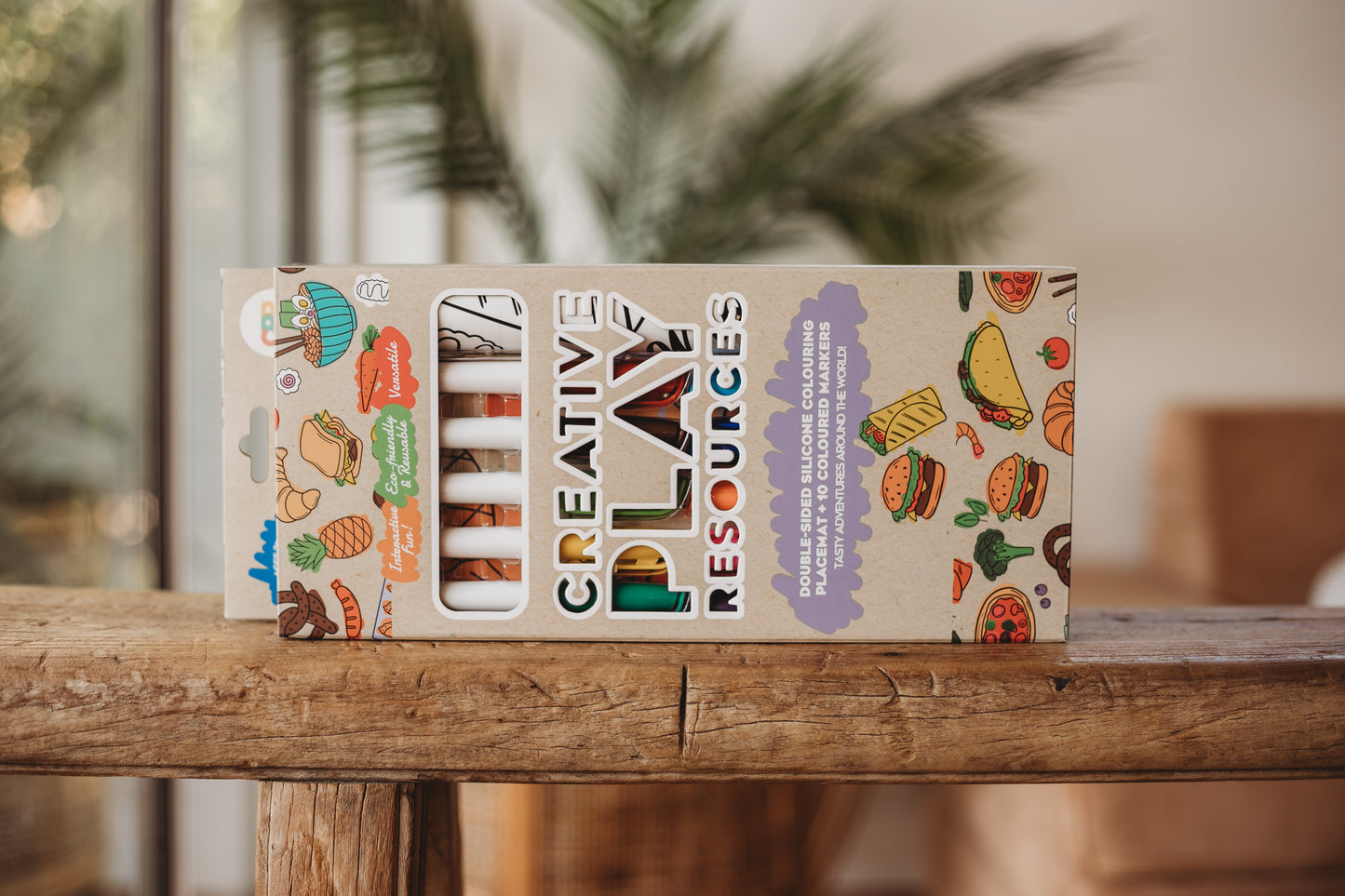 Box of Creative Play Resources silicone colouring mat on a wooden surface with blurred greenery in the background