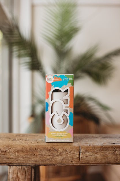 Colorful packaging of a children's drinking cup on a wooden surface with a blurred plant background