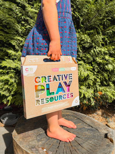 Child holding a 'Creative Play Resources' box outdoors