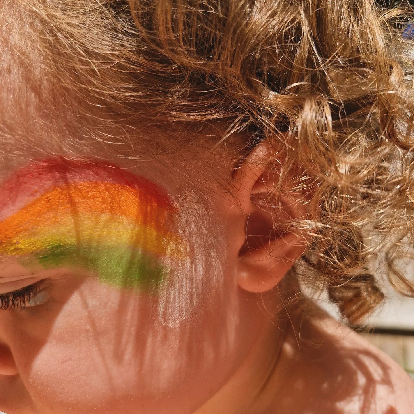 a young child with rainbow coloured face painting on her face using non-toxic CPR face paint sticks that are twistable like a crayon and easy to use. They wash off easily with water.