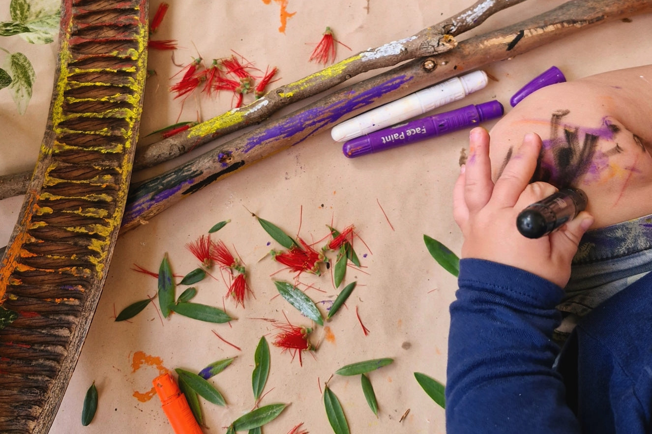 young child drawing on their body with colourful non-toxic face and body paint sticks.