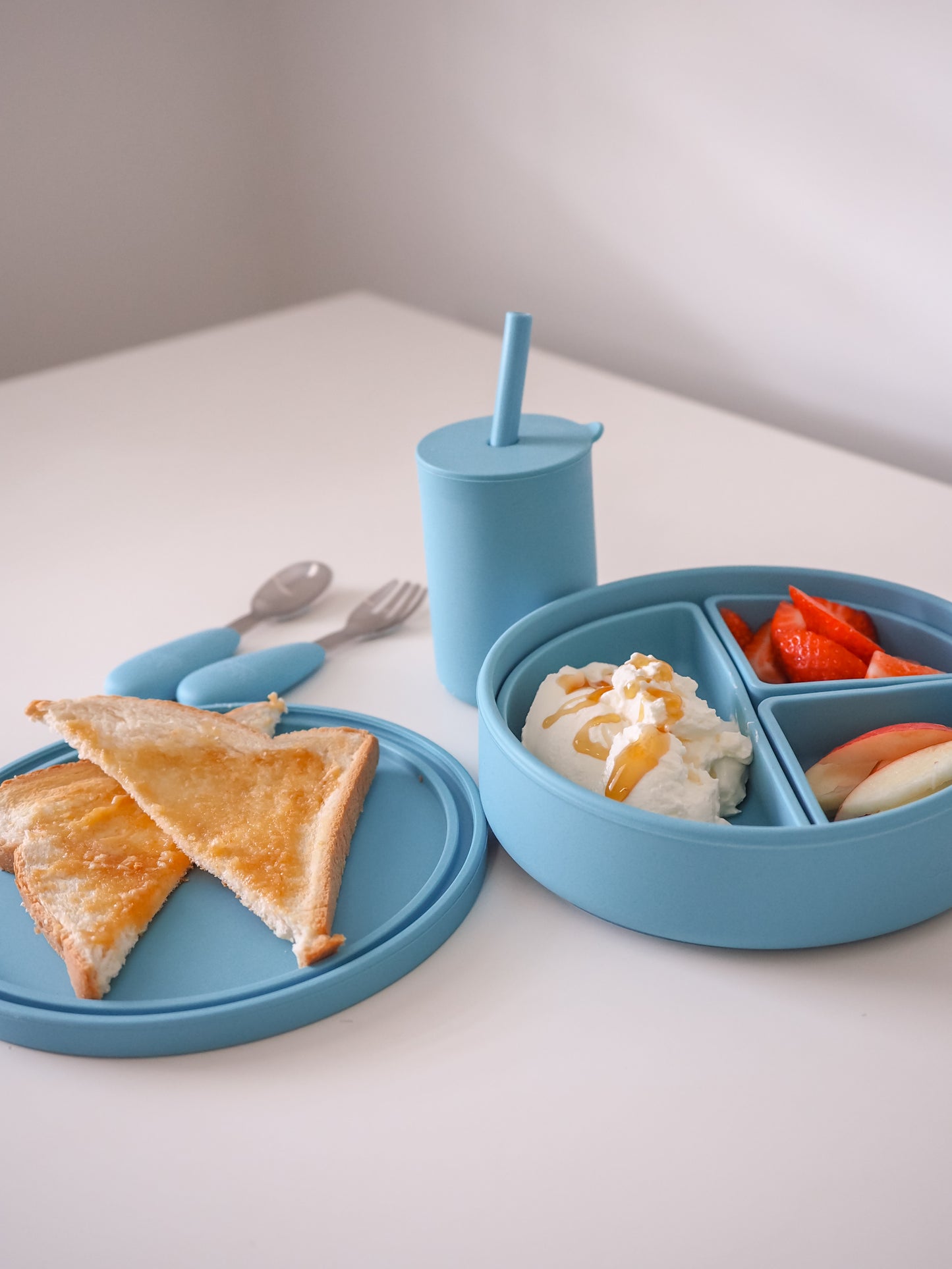 Blue children's meal set with plate, cup, and bowl on a white surface