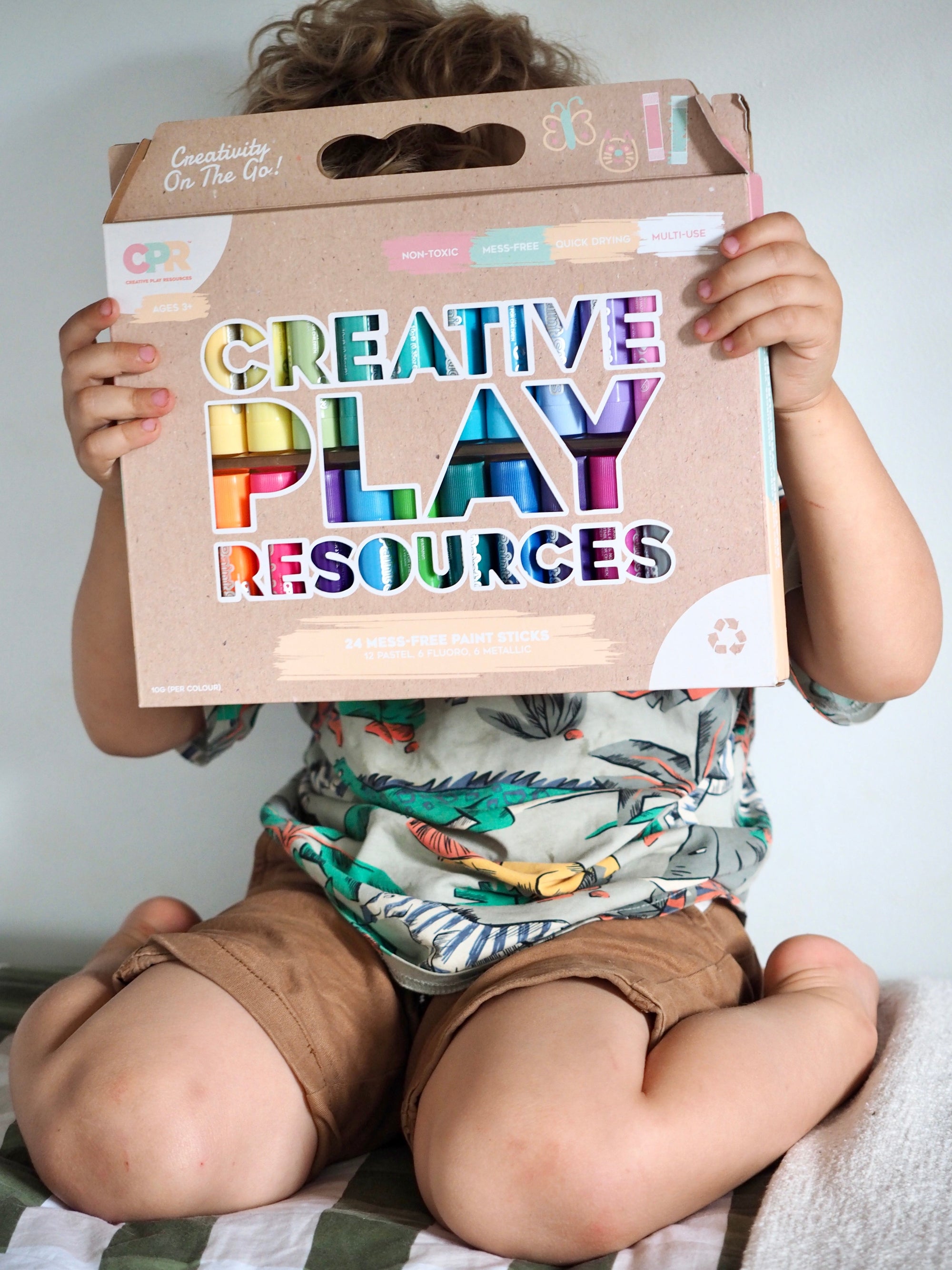 Child holding a cardboard box labeled 'Creative Play Resources' with colorful text.