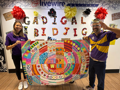 Two people holding a colorful quilt in front of a wall with 'Livewire' and 'Gadigal Bidjigal' text.