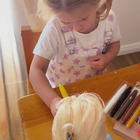 girl drawing with face paint sticks on dolls and her face
