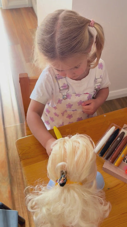 girl drawing with face paint sticks on dolls and her face